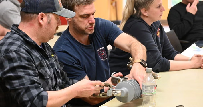 Unitil employees sit at a table and hold an electric component in a learning session