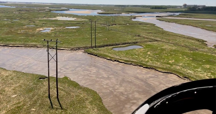 aerial view of a grassy marsh with a waterways and a view of electrical powerlines and poles