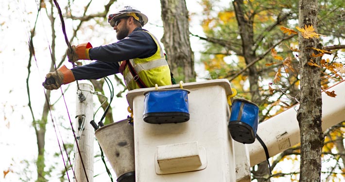 closeup of lineworker fixing utility line with tress in background