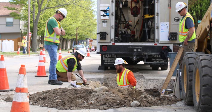 workers in and surrounding an excavation site in the street blocked by street cones